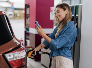 woman at gas station pumping gas while checking her phone